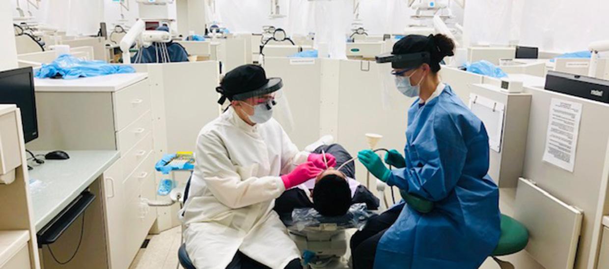 Dental assisting student helping professor work on a patient
