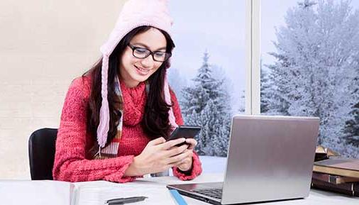 女学生在家学习，穿着毛衣，用手机，笔记本电脑放在桌子上